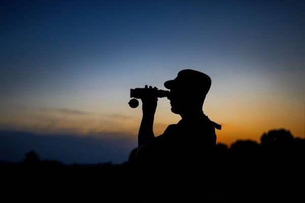 In this Friday July 9 2021 file photo a member of the Lithuania State Border Guard Service looks through binoculars as he patrols on the border with Belarus